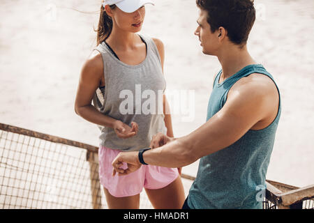 Coppia giovane a discutere le prestazioni di allenamento durante la pausa di allenamento all'aperto. Guide di scorrimento con monitor per la frequenza cardiaca sulla spiaggia. Foto Stock