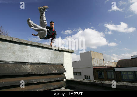 Un parkour freerunning atleta volteggia sopra un muro su un tetto con cielo blu in background Foto Stock