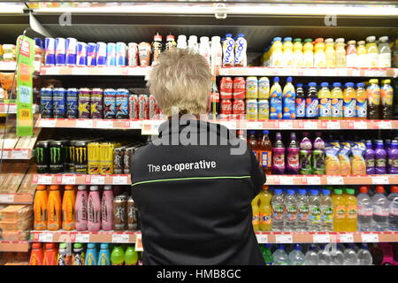 Il personale del negozio ripiano impilaggio in una cooperativa locale store Foto Stock