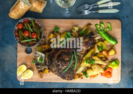 Arrosto di agnello gambo con patate arrosto e carote in stile rustico di legno, vista dall'alto Foto Stock