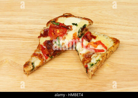 Formaggi saporiti su toast, mozzarella, formaggi cheddar con pancetta, pomodoro e basilico su marrone seminate il pane su un tagliere di legno Foto Stock