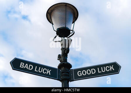 Street palo di illuminazione con due opposte frecce direzionali blu su sfondo nuvoloso. Sfortuna versus buona fortuna concetto. Foto Stock