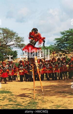 Danzatori Dogon, uno di essi su palafitte, indossando maschere Kanaga eseguendo la Dama o mascherato danza funebre, Bandiagara scarpata, Foto Stock