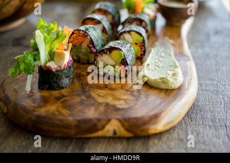 Materie vegan nori rotoli a mano di colore rosa con salsa di rafano, insalata e verdure. Su una lastra di ardesia contro uno sfondo di legno. Vegetariano senza glutine foo Foto Stock