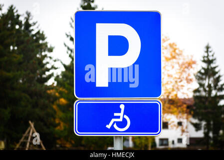 Simbolo della carrozzella in un parcheggio disabili contrassegni di parcheggio. Iconon bianco blu quadrata in metallo segno. Foto Stock