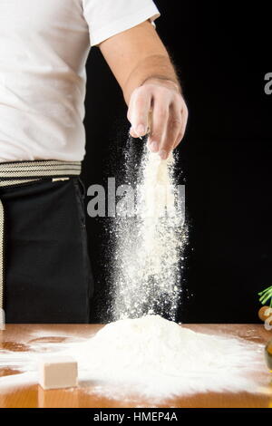 Voce maschile baker aggiungendo farina sulla pila a mano Foto Stock