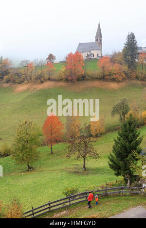 La nebbia e coloratissimi alberi circondano la chiesa Alpina in autunno, Maddalena, Val di Funes, Alto Adige, Dolomiti, Italia Foto Stock