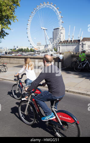 Uomo di mezza età e la donna in sella Santander biciclette a noleggio su est-ovest il superhighway di ciclo con il London Eye in background sul giorno di estate a Londra Foto Stock