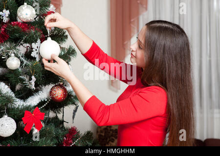 X-mas, vacanze invernali e concetto di persone - felice giovane donna decorazione di albero di natale con sfera a casa Foto Stock