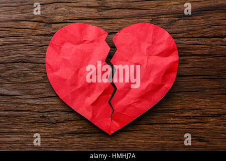 Man mano che tiene una carta rossa cuore spezzato su sfondo di legno Foto Stock