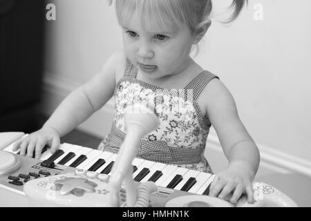 Bimba bionda bambino kid giocando sulla tastiera, pianoforte grave, tre anni di imparare la musica canto lezioni di gioco divertente il concetto di famiglia Foto Stock