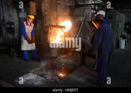 Foundrymen pour ferro fuso da un forno ad induzione in ladel presso una piccola fonderia. (Shot in luce disponibile con profondità di campo). Foto Stock