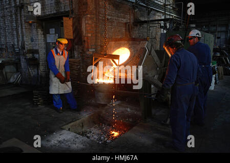 Foundrymen pour ferro fuso da un forno ad induzione in ladel presso una piccola fonderia. (Shot in luce disponibile con profondità di campo). Foto Stock