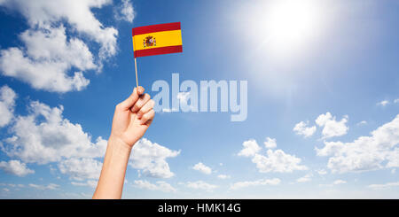 Mano di donna che tiene bandiera spagnola contro il cielo blu Foto Stock