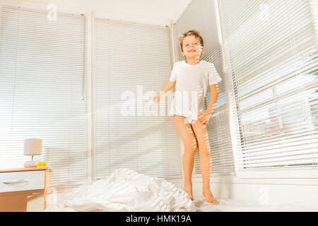 Ragazzo carino che salta sul suo letto al mattino soleggiato Foto Stock