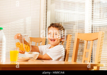 Ragazzo versando fiocchi di mais facendo una colazione sana Foto Stock