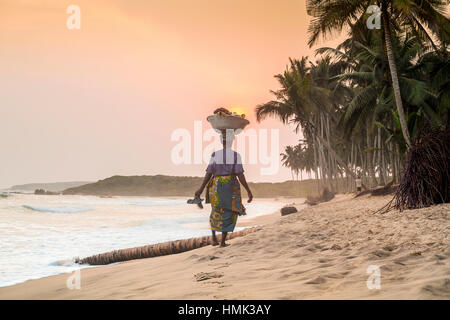 Donna locale che trasportano merci sulla sua testa, Spiaggia, Tramonto, fiume Volta, Ghana Foto Stock