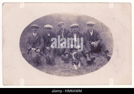 Cartolina dei primi del 1900 di giovani uomini lavoranti e un cane in campagna con cappelli e giacche piatte, possibilmente in una gita di un giorno. Regno Unito circa 1905 Foto Stock