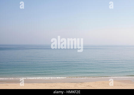 Mare calmo e cielo blu con piccole onde che si infrangono sulla spiaggia sabbiosa Foto Stock