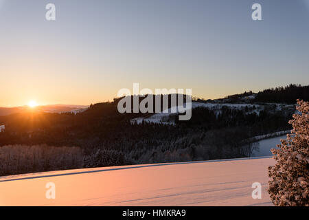 Luminosa alba invernale, campo innevato, valle, cielo azzurro, luce dorata, vista panoramica verso l'orizzonte su un'idilliaca campagna naturale Foto Stock