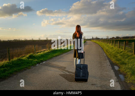 Runaway girl in piedi con la sua valigia sulla strada e cercare l'ultima volta al suo villaggio nativo Foto Stock