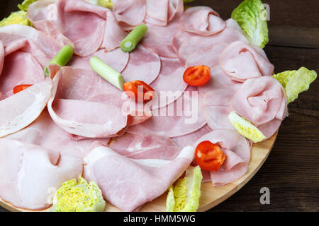 Vassoio per alimenti con deliziosi salami, pezzi di fette di prosciutto, pomodori, insalata e ortaggi - piatto a base di carne con selezione Foto Stock