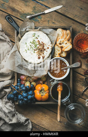 Formaggi, frutta, vino impostato nel vassoio di legno su sfondo rustico Foto Stock