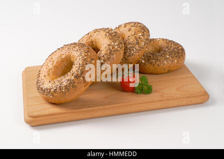 Bagel freschi e rabboccato con semi sul tagliere di legno Foto Stock