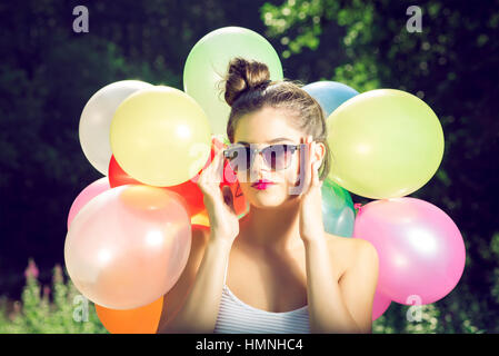 Ragazza con palloncini in natura rendendo le espressioni del viso Foto Stock