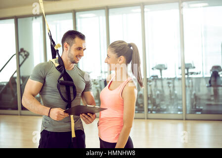 Personal trainer che mostra il risultato di un piano di formazione per i suoi giovani femmine client con corda di sospensione sulla spalla. Foto Stock