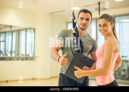 Personal trainer che mostra il risultato di un piano di formazione per i suoi giovani femmine client con corda di sospensione sulla spalla. Foto Stock