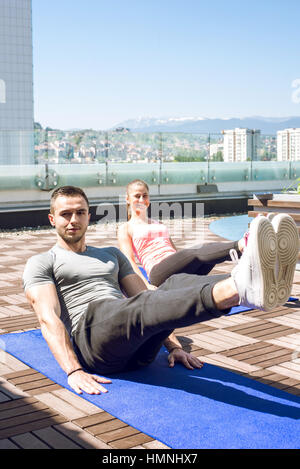 Giovane coppia fitness facendo gambe sgranocchia all'aperto sul tetto. Foto Stock