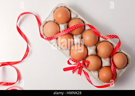 Uova di colore marrone in una confezione di uova con il rosso e bianco polka dot ribbon e prua su sfondo bianco. Vista superiore Foto Stock