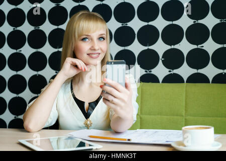 Ragazza seduta in cafe contiene uno smartphone Foto Stock