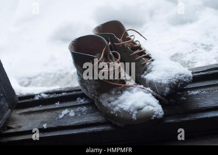 Vista in pianta di una coppia di pelle marrone vintage scarpe dalla casa di legno aperto della porta d'ingresso coperto di neve in inverno Foto Stock