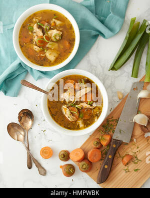 La Turchia o pollo riso e zuppa di verdure servita in due ciotole bianco. Un tagliere, coltello e i resti di un trito di verdure sono state sparse Foto Stock