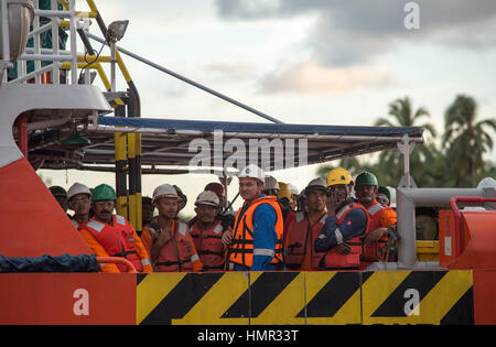 Gli operatori petroliferi in tute arancioni sono visti transformarsi dalle piattaforme offshore di perforazione petrolifera tramite navi di supporto al porto vicino a Kuala Belait, Brunei. © Time-Snap Foto Stock