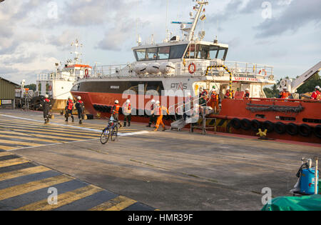 Gli operatori petroliferi in tute arancioni sono visti transformarsi dalle piattaforme offshore di perforazione petrolifera tramite navi di supporto al porto vicino a Kuala Belait, Brunei. © Time-Snap Foto Stock