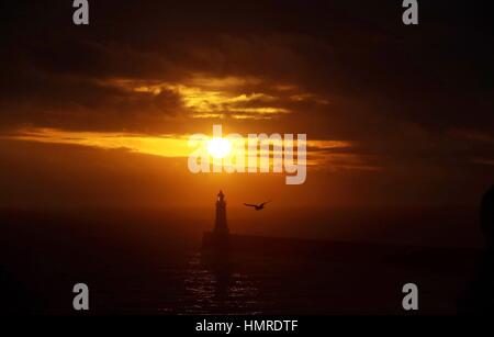 Il sole sorge al molo di Tynemouth e faro sulla costa nord est. Foto Stock