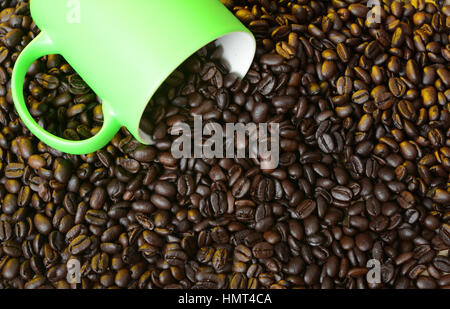 Chicchi di caffè tostati fuoriuscita di tazza verde. Foto Stock