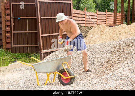 Uomo di ghiaia di caricamento in una carriola con una pala Foto Stock