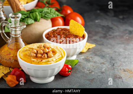 In casa hummus e salsa di pomodoro in bianco ciotole con verdure e corn chips Foto Stock