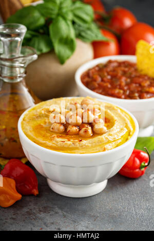 In casa hummus e salsa di pomodoro in bianco ciotole con verdure e corn chips Foto Stock