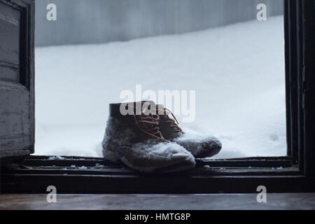 Vista frontale di una coppia di pelle marrone vintage scarpe dalla casa di legno aperto della porta d'ingresso coperto di neve in inverno Foto Stock