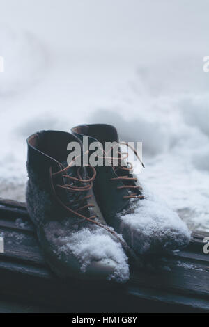 Verticale vista frontale di una coppia di pelle marrone vintage scarpe dalla casa di legno aperto della porta d'ingresso coperto di neve in inverno Foto Stock