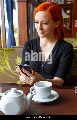 Ritratto di bella ragazza in hat usando il suo telefono cellulare in cafe. Tonned. Messa a fuoco selettiva. Foto Stock