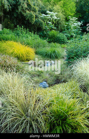 Letto di erbe in primavera con un contenitore per l'acqua, Jardins du pays d'Auge, Normandia, Francia Foto Stock