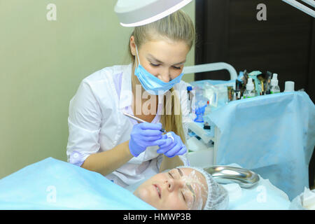 Giovane donna bionda professional, impegnati nel lavoro di ricostruzione responsabilmente, sopracciglia metodo manuale esegue la procedura, utilizzando ago più sottile e mani Foto Stock