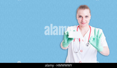 Femmina gioiosa medic mostra biglietto da visita e fare ok gesto su sfondo blu con copyspace Foto Stock