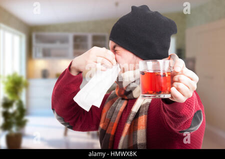 Giovane uomo con la tazza di tè soffia il naso come raffreddore e influenza concetto in casa Foto Stock